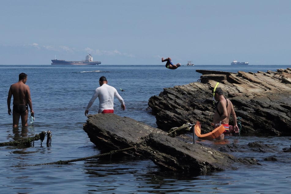 People wade by rocks and dive into the sea near Keelung on August 4, 2022, as China held military exercises encircling Taiwan.