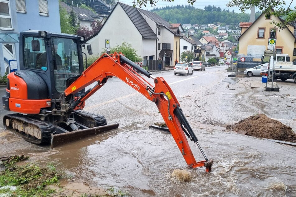 Mit einem kleinen Bagger wird in Schriesheim-Altenbach versucht, den Bestbach freizuschaufeln, um das Wasser von der überfluteten Straße abfließen zu lassen.