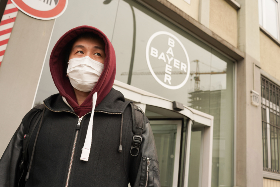 Ein Mann mit Mundschutz geht an einem Logo des Chemiekonzerns Bayer vorbei. 