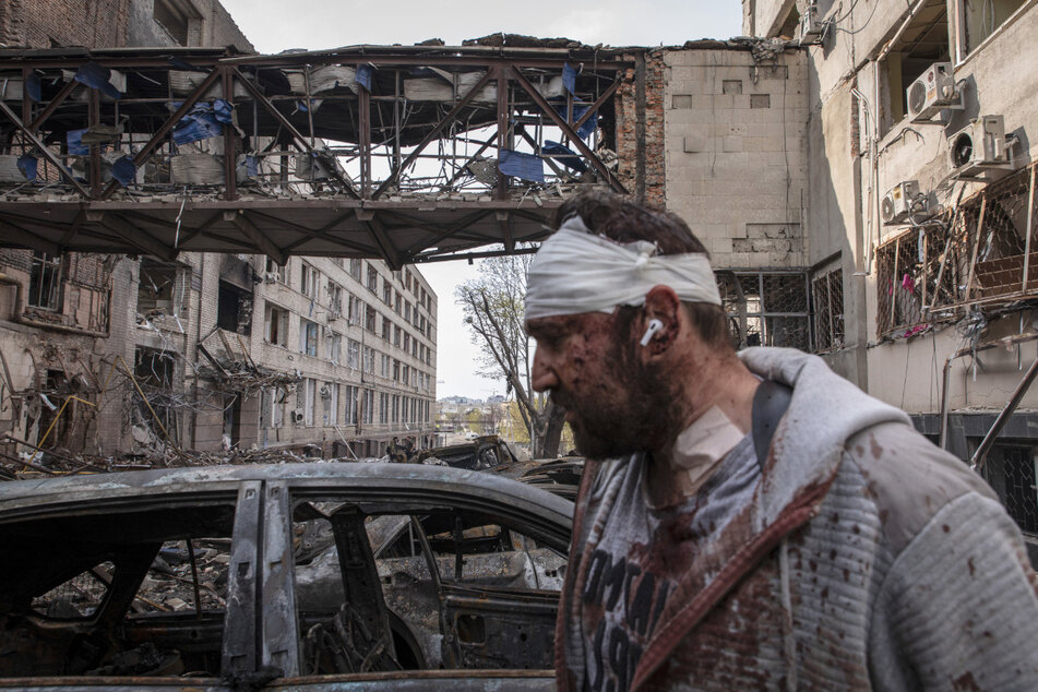 Ein verletzter Mann geht an durch Beschuss zerstörten Gebäuden in Charkiw vorbei.