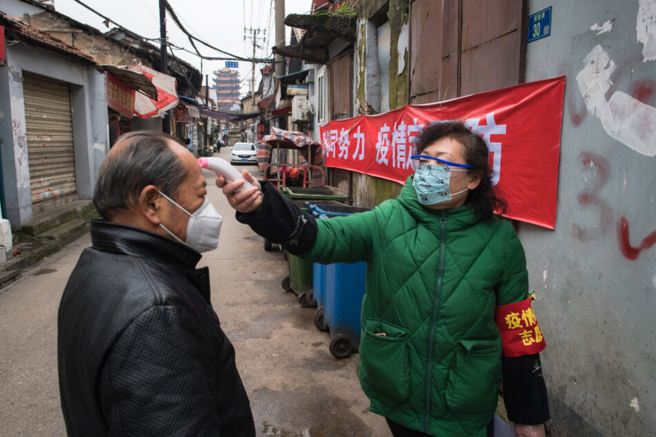 Eine Gemeindemitarbeiterin misst die Körpertemperatur eines Passanten in Wuhan, Anfang Februar 2020.