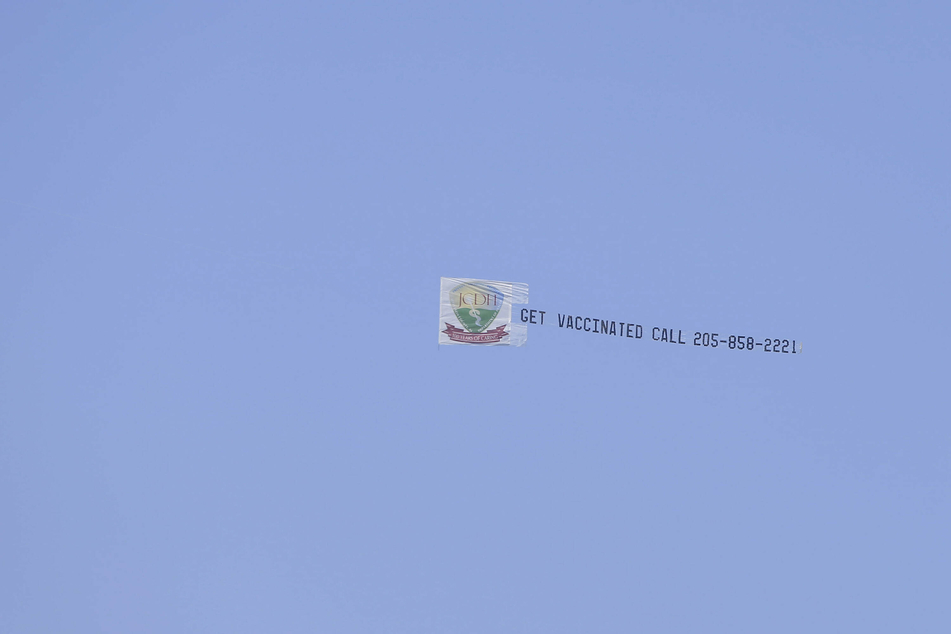 A banner calling for Vaccines flies behind an airplane during warm ups for the Honda Indy Grand Prix of Alabama.