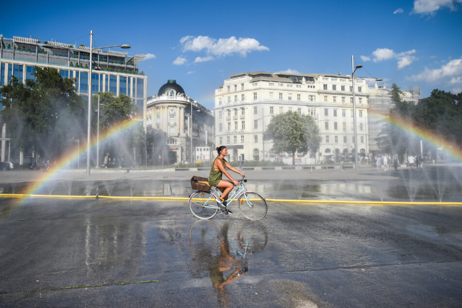 Österreich, Wien: Ein Radfahrerin kühlt sich in der Nähe einer Wasserinstallation auf dem Schwarzenbergplatz ab.