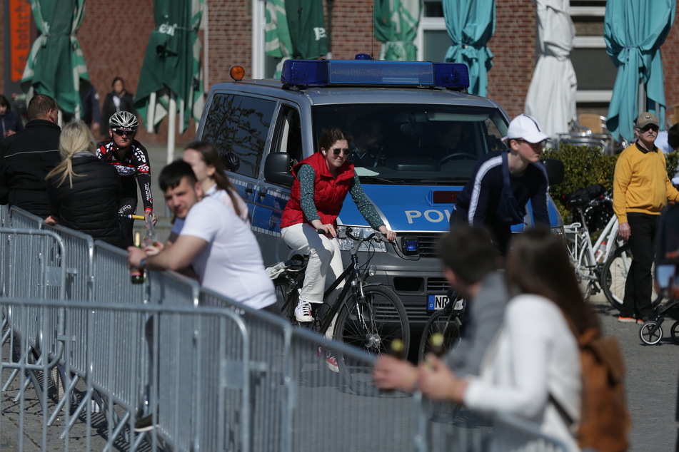 Ein Polizeiwagen fährt zwischen vielen Menschen am Düsseldorfer Rheinufer Streife.