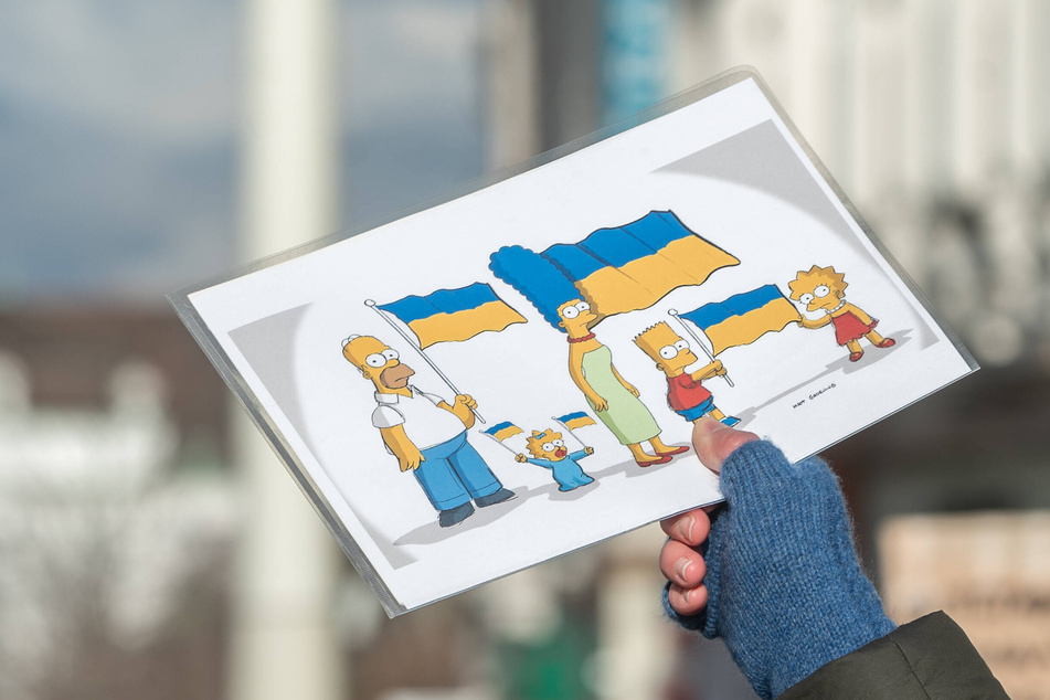 A protester holds up an image of the Simpsons characters waving Ukrainian flags.