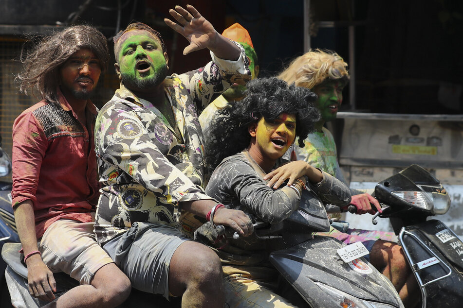 Jugendliche sitzen beim Frühlingsfest "Holi" mit durch Farbe beschmierten Gesichtern auf einem Moped.