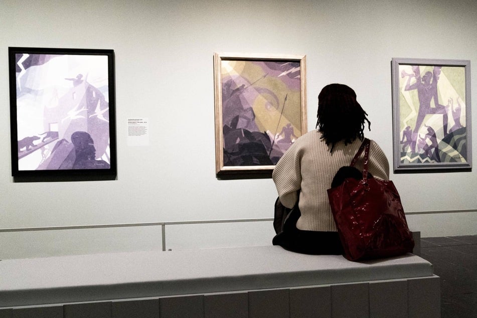 A visitor looks at paintings by Aaron Douglas with Let My People Go in the middle at the Harlem Renaissance Exhibition.