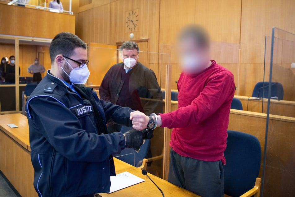 Ein Justizwachtmeister nimmt dem Angeklagten Alexander M. (54) im Prozess um die "NSU 2.0"-Drohschreiben die Handschellen ab. Im Hintergrund steht Verteidiger Marcus Steffel.