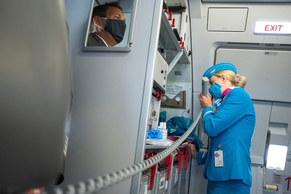 Eine Flugbegleiterin mit Mund- und Nasenschutz spricht bei der Fluggesellschaft Eurowings in die Sprechanlage.