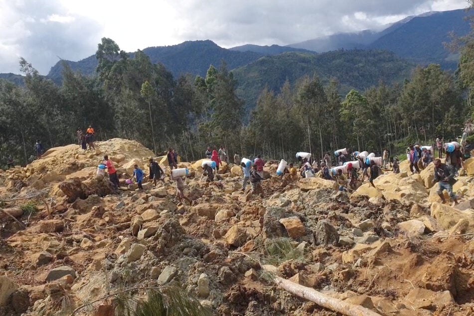 People carry bags in the aftermath of a landslide in Enga Province, Papua New Guinea.