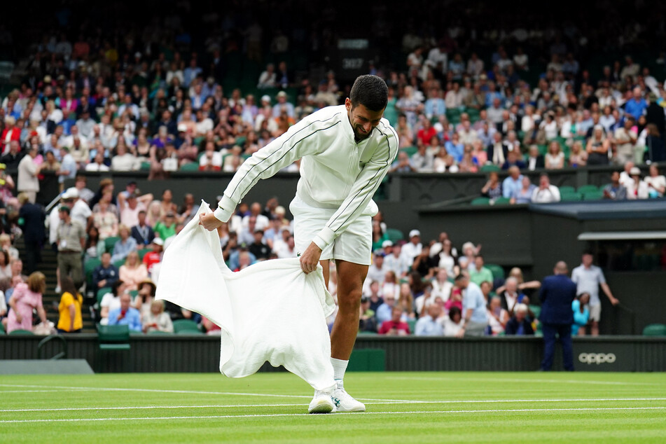 Kurioses Bild: Topstar Novak Djokovic (36) versucht den nassen Rasen im "Tempel des Tennis" mit einem Handtuch zu trocknen.