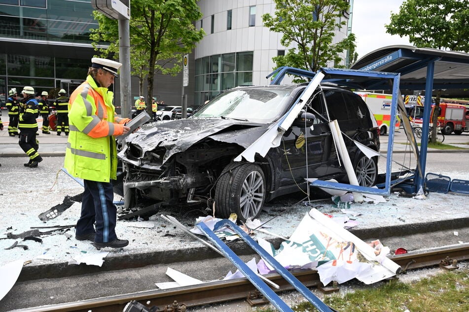 Ein Polizist steht neben dem Unfallfahrzeug in den Glassplittern der Haltestelle.