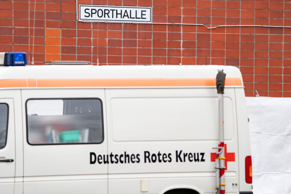 Ein Fahrzeug des Roten Kreuzes steht vor einer Sporthalle.