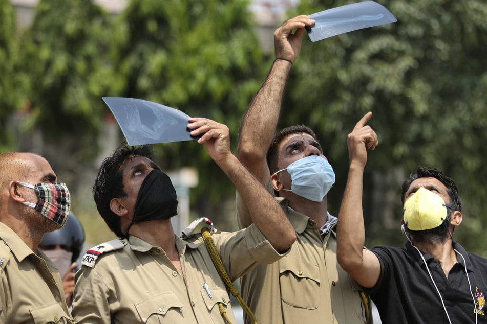 Indien, Jammu: Männer, die als Schutzmaßnahme gegen das Coronavirus Mundschutze tragen, beobachten in Jammu eine partielle Sonnenfinsternis durch Röntgenaufnahmen hindurch, um die Augen vor Strahlung zu schützen.