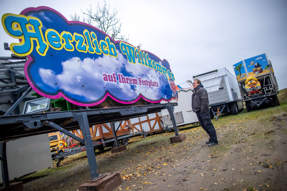 Marco Welte steht auf dem Firmengelände der Schausteller-Familie Welte vor dem Eingangstor für einen Festplatz mit der Aufschrift "Herzlich Willkommen".