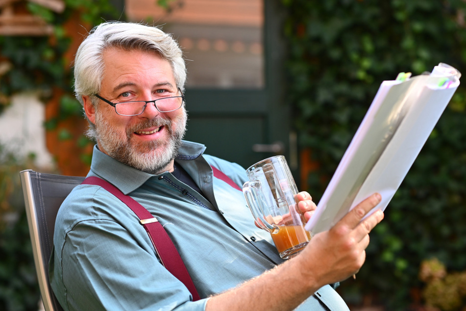 Schauspieler Dieter Fischer (50) sitzt mit einem Drehbuch und einer Saftschorle in seinem Garten.