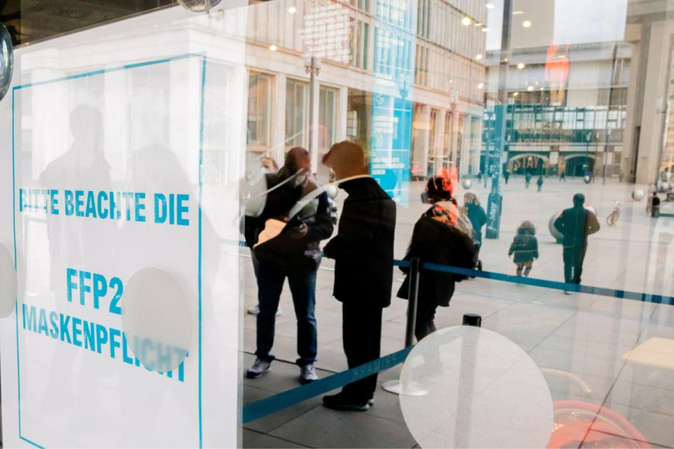 Ein Hinweisschild zum Beachten der FFP2-Maskenpflicht hängt am Eingang eines Bekleidungsgeschäftes am Alexanderplatz.