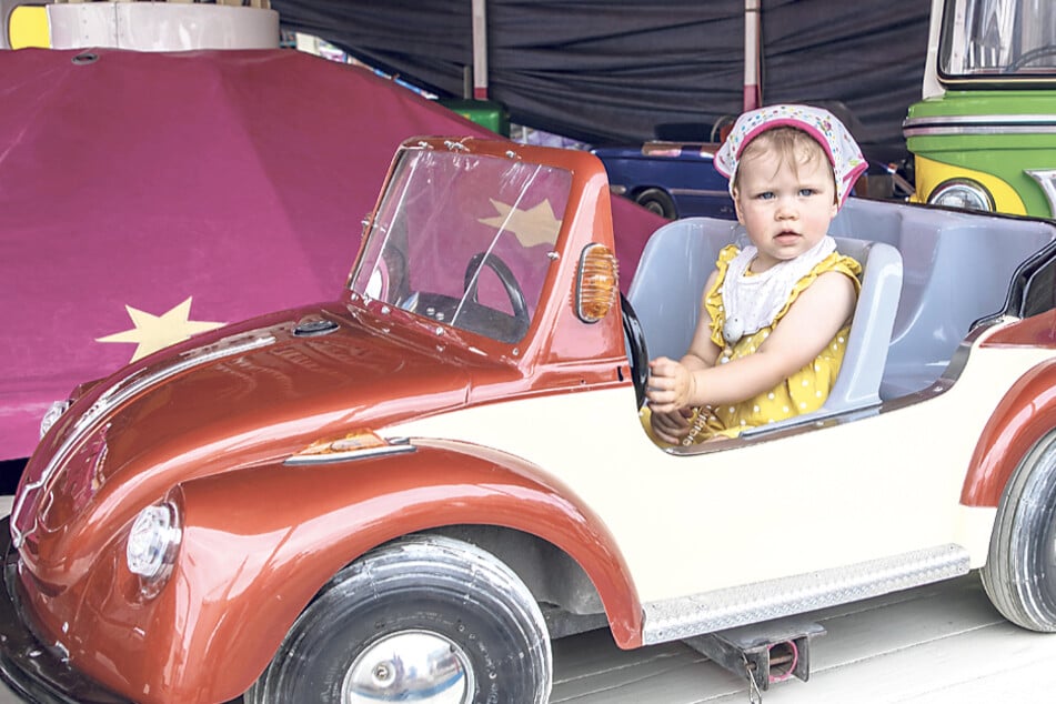 Die kleine Ellie (16 Monate) hat sich im DDR-Kinderkarussell hinters Lenkrad eines Cabrios gesetzt.