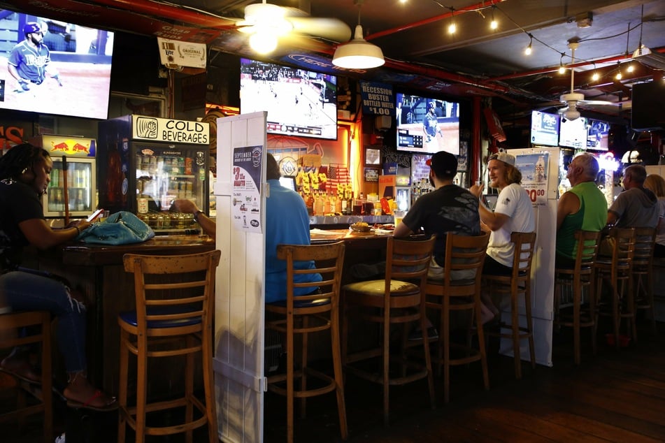 USA, St. Petersburg: Baseballfans in der Ferg's Sports Bar verfolgen das Spiel der Tampa Bay Rays gegen die New York Yankees. Wegen der Corona-Pandemie gibt es in vielen Bars Vorrichtungen, um den Mindestabstand zu gewähren.