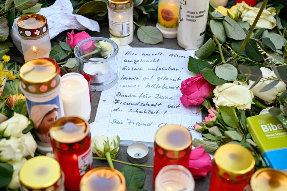 Ein beschriebener Zettel liegt auf der Einkaufsstraße Planken zwischen niedergelegten Blumen und Kerzen in Mannheim.