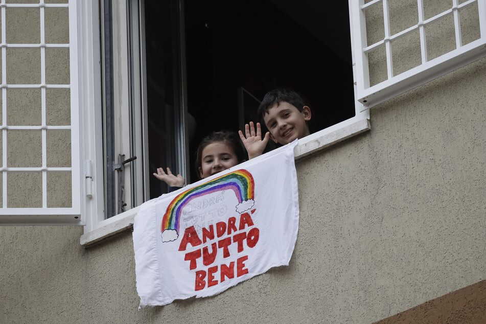 Zwei Kinder in Italien hängen einen Banner mit der Aufschrift "Alles wird gut" aus dem Fenster.
