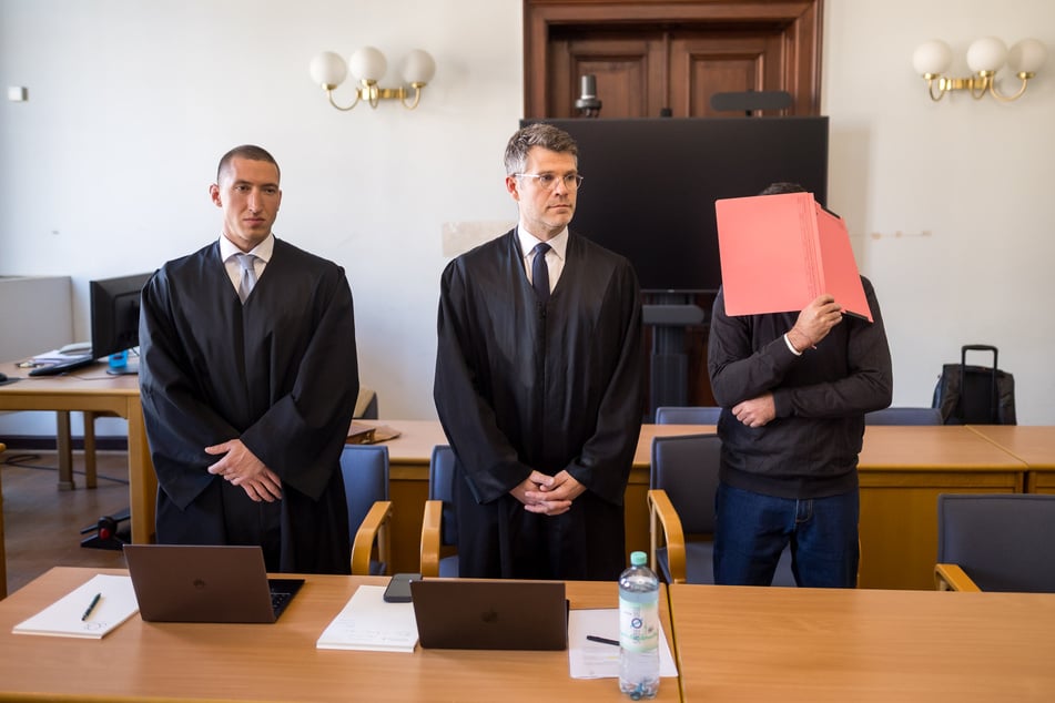 Der mutmaßliche Millionenbetrüger Adam K. (41), hier mit zwei seiner vier Anwälte, verbirgt vor Gericht sein Gesicht.