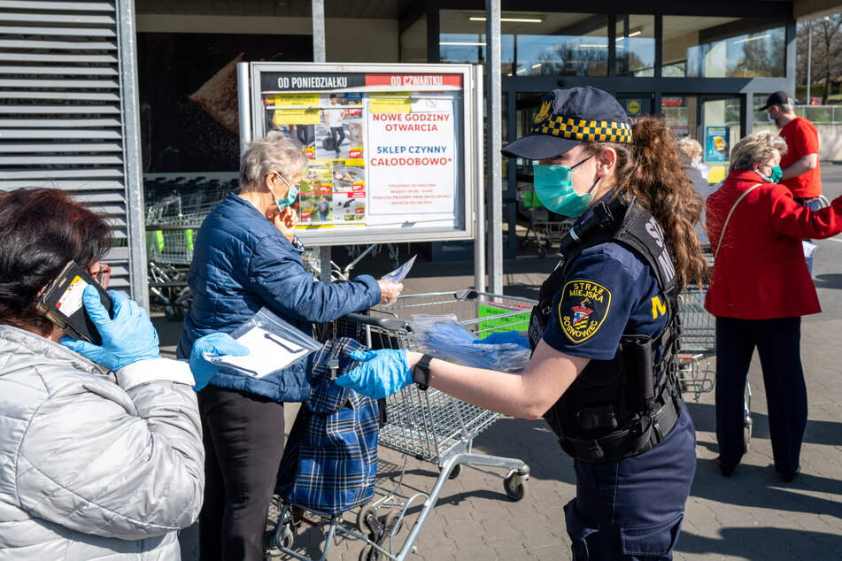 Ein Mitglied der Stadtpolizei verteilt Schutzmasken an Seniorinnen vor einem Supermarkt in Sosnowiec. In der ganzen Stadt werden von Mitgliedern der freiwilligen Feuerwehr, der Stadtwache und Freiwilligen zehntausende Schutzmasken verteilt.