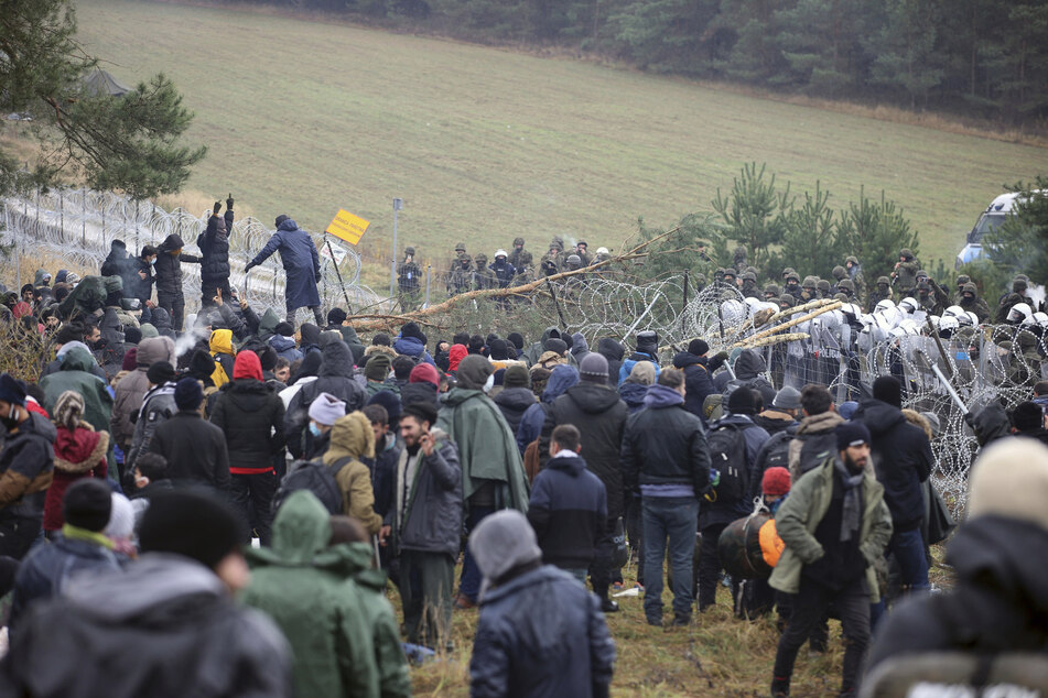 Polnische Polizisten stehen hinter einem Stacheldrahtzaun, während sich an der belarussisch-polnischen Grenze Migranten versammelt haben.