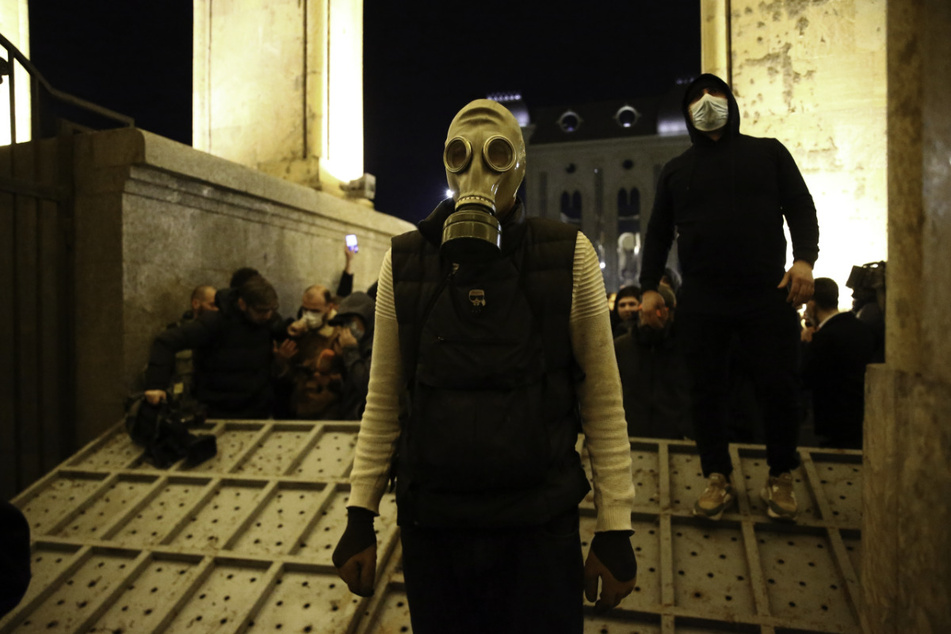 Demonstranten, von denen einer eine Gasmaske trägt, versammeln sich an einem zerstörten Sicherheitszaun vor dem georgischen Parlamentsgebäude.