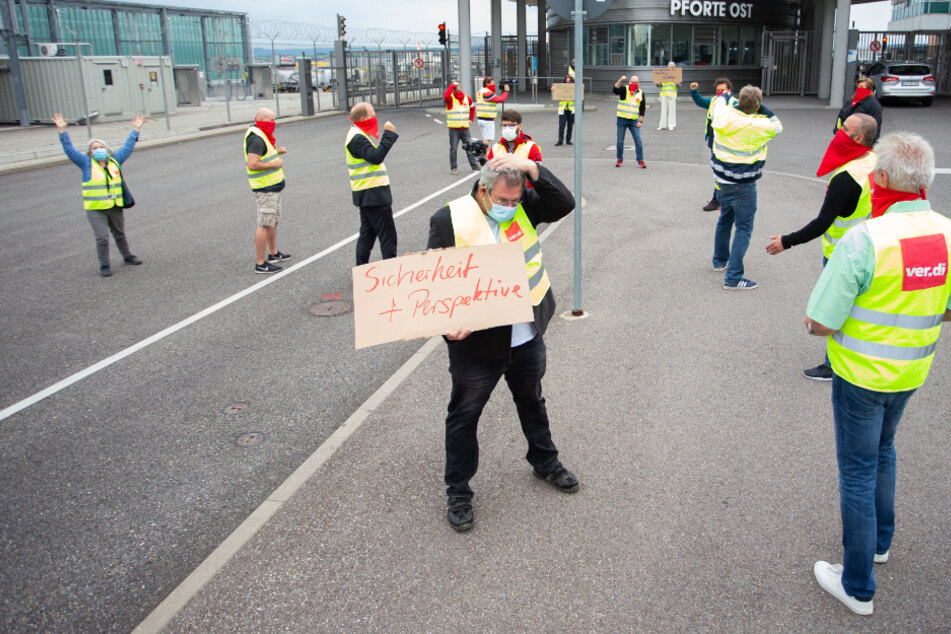 Demonstranten stehen bei der Aktion "Freeze" vor dem Stuttgarter Flughafen. Ein Demonstrant hat ein Schild mit der Aufschrift "Sicherheit + Perspektive" in der Hand.