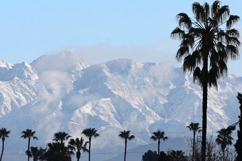 Palm trees stand in front of the snow-covered San Gabriel Mountains in Los Angeles, California.