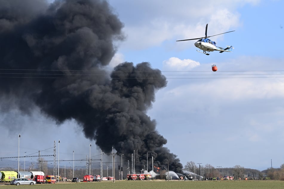 Ein Löschhubschrauber fliegt am Freitag, dem 28. Februar 2025 zum Unfallort, während Einsatzkräfte vor Ort arbeiten.