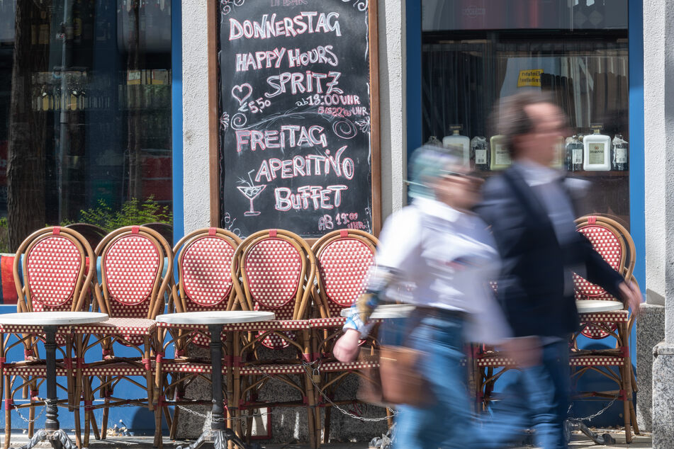 Passanten gehen an zusammengestellten Tischen und Stühlen eines geschlossenen Cafes vorbei. (Archivbild)