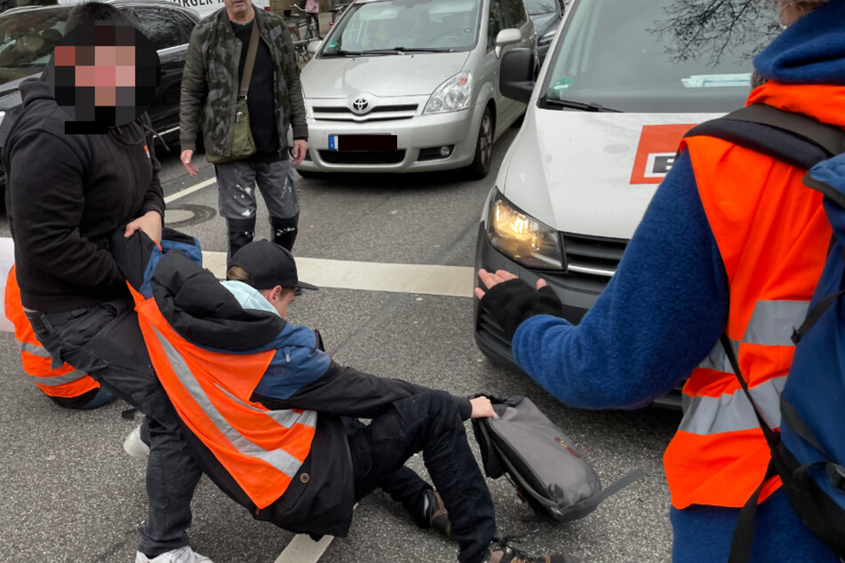 Eine Person versucht einen Aktivisten von der Straße zu entfernen.