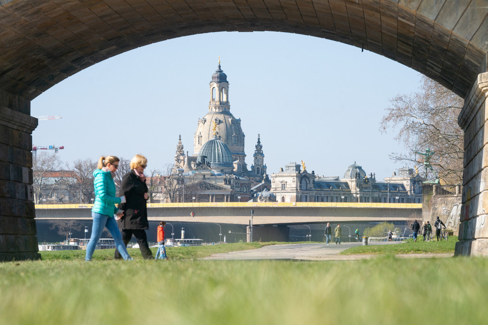 Zwei Frauen gehen in den Dresdner Elbwiesen spazieren. Im Hintergrund ist die Dresdner Frauenkirche zu sehen.