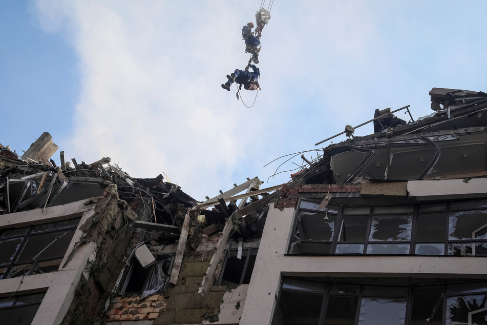 Ukrainian rescue workers riding the lifting hook of a crane above the Kyiv building damaged by a Russian missle strike.