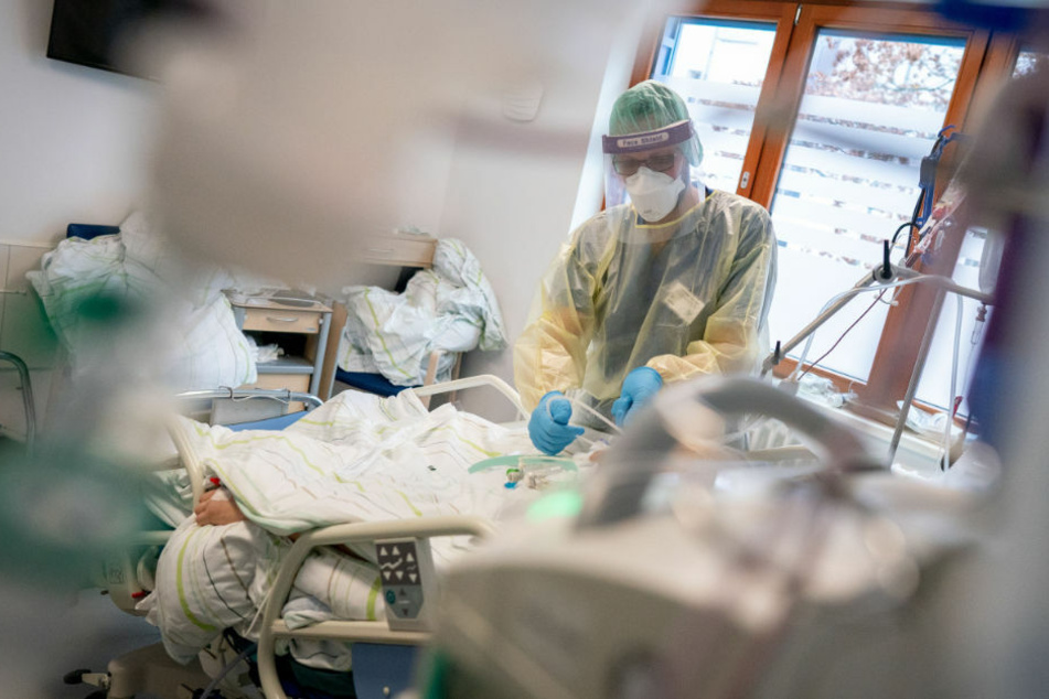 Ein Intensivpfleger arbeitet in einer Schutzausrüstung mit Mund-Nasenbedeckung, Gesichtsschutz, Kittel und Haube auf der Intensivstation eines Krankenhauses an einem Corona-Patienten. (Symbolfoto)