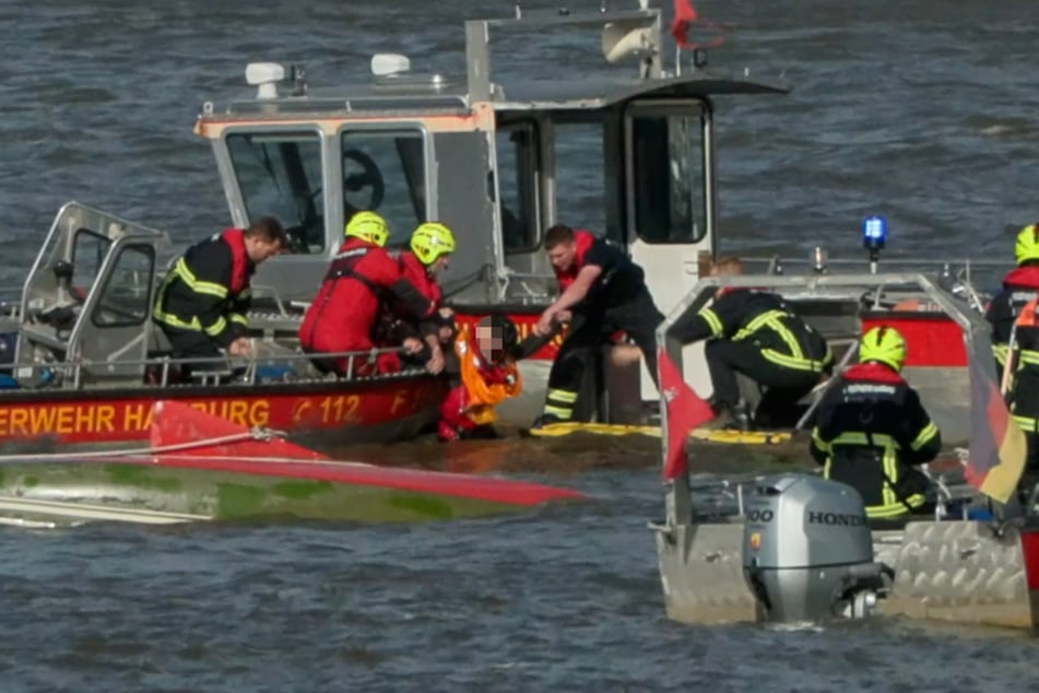 Einsatzkräfte der Feuerwehr retten einen Mann (M.) aus der Elbe. Das kleine Segelboot schwimmt kieloben im Wasser.