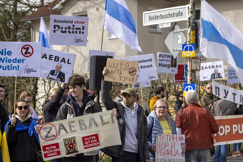 Demonstranten stehen auf der anderen Straßenseite des russischen Generalkonsulats in Bonn und protestieren gegen Präsident Putin.