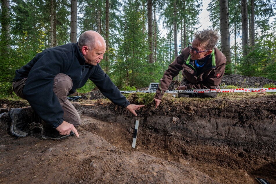 Heide Hönig und Frank Schröder zeigen die Ablagerungsschichten des archäologischen Profils.