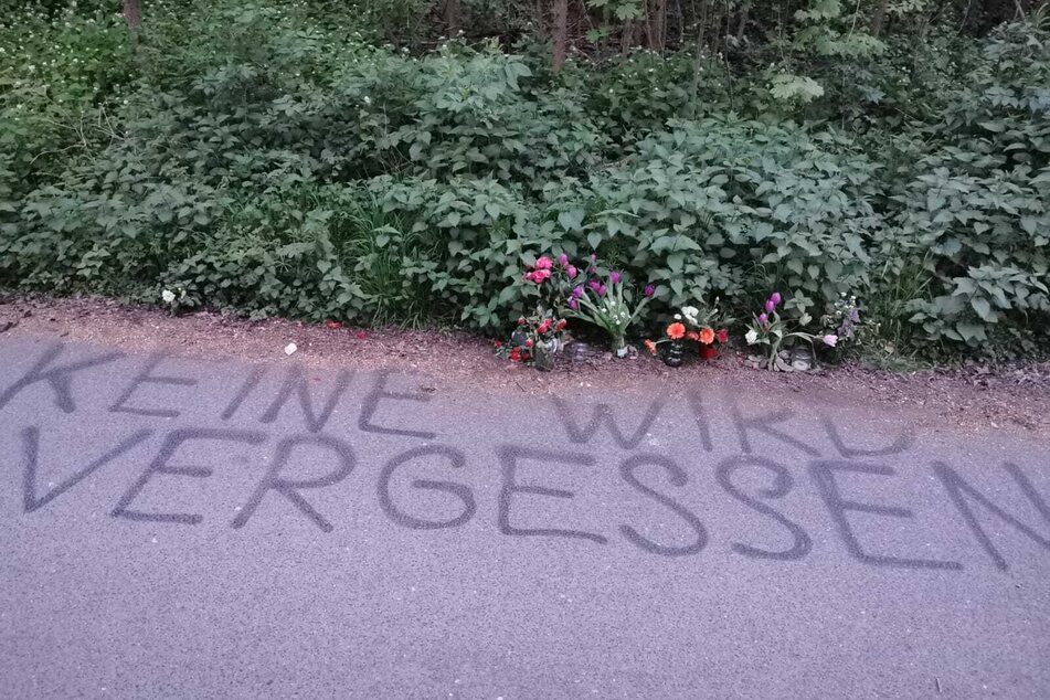 An dem belebten Auwald-Weg steht groß "Keine wird vergessen", mehrere Blumen wurden platziert.