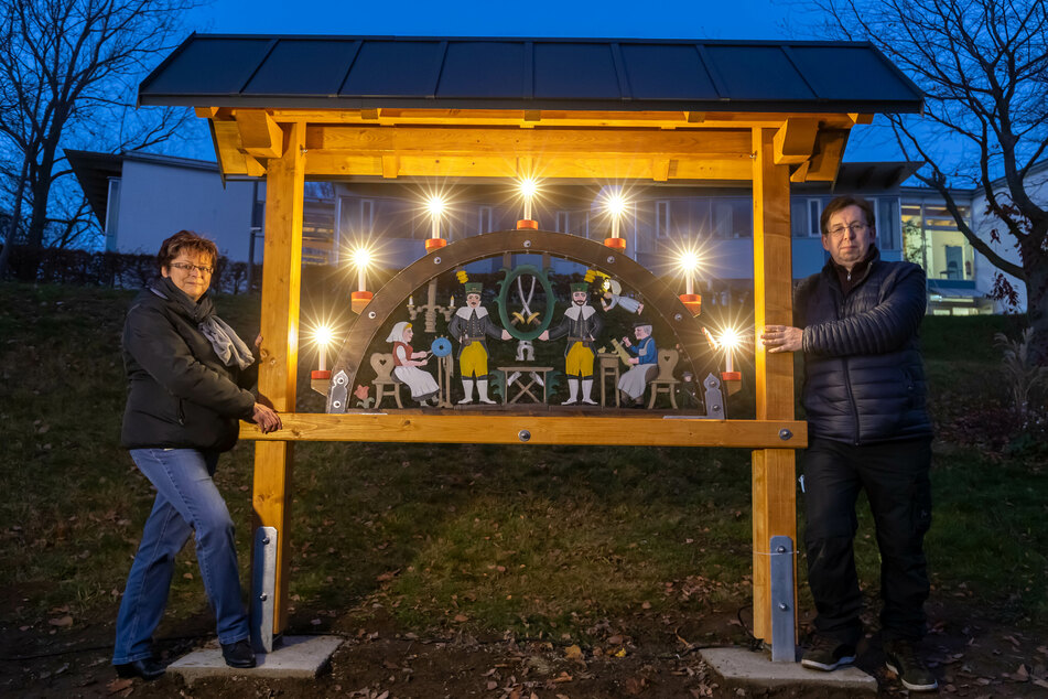 Jana Rollinger (56), Leiterin der Ergotherapie, und der ehemalige Patient Steffen Götz (63) stehen am neuen Schwibbogen am Erzgebirgsklinikum.