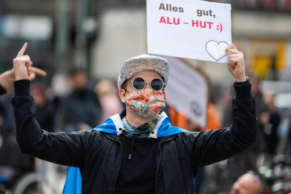 Auf dem Alexanderplatz steht in einem abgesperrten Bereich ein Demonstrant mit einem Schild mit der Aufschrift "Alles gut, Alu-Hut".