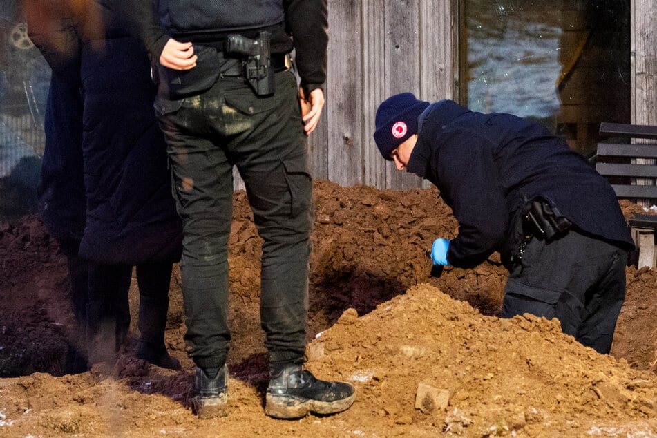 Ermittler der Polizei arbeiten hinter einem Mehrfamilienhaus in Mölln in einem Garten an einem Erdloch. Dort wurde am Montag eine vergrabene Leiche gefunden.