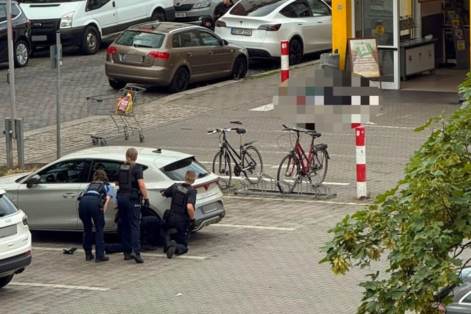 Polizisten suchen Deckung hinter einem geparkten Auto. Direkt vorm Netto-Eingang liegt der Tatverdächtige in seinem eigenen Blut.