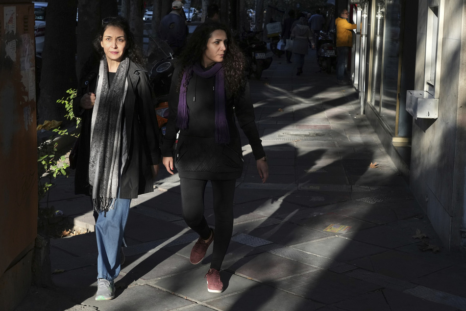 Iran, Tehran: Zwei iranische Frauen gehen auf einem Bürgersteig, ohne ihr vorgeschriebenes islamisches Kopftuch zu tragen.