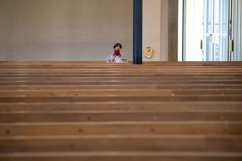 Eine Frau mit Mundschutz verfolgt einen Gottesdienst in der ansonsten fast menschenleeren St. Matthäuskirche.