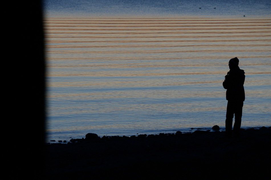 Ein Mann steht in Friedrichshafen bei Sonnenuntergang am Ufer des Bodensees. (Illustration)