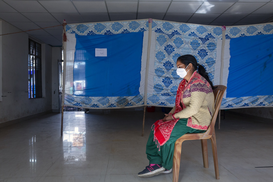 Indien, Dharmsala: Eine Freiwillige sitzt vor einem Beobachtungsraum auf einem Stuhl, nachdem sie an einer Corona-Testimpfung teilgenommen hat. In Indien soll am 16.01.2021 eine der weltweit größten Corona-Impfkampagnen beginnen.
