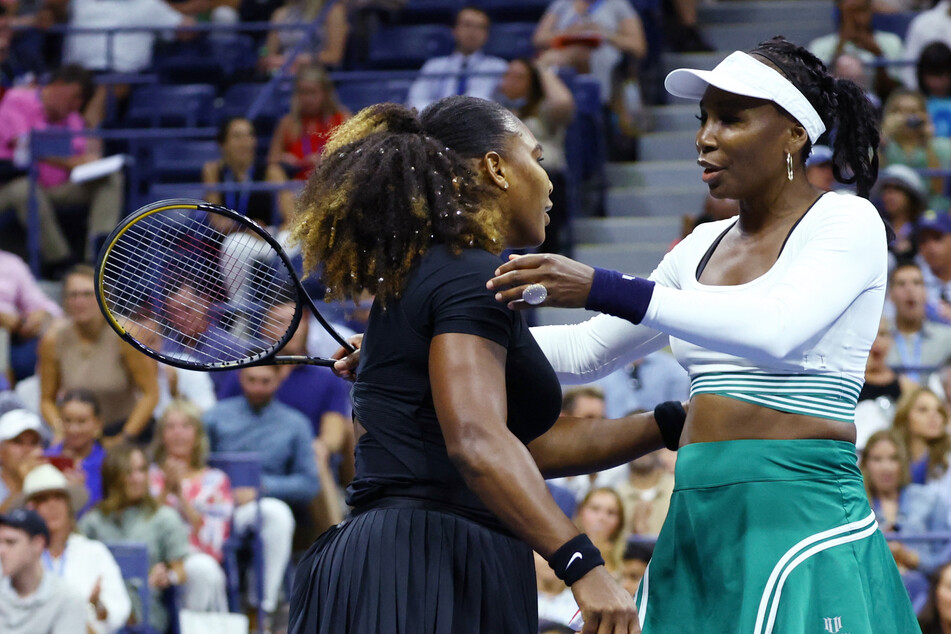Serena (l.) and Venus Williams hug after losing their women's doubles first-round match at the 2022 US Open.